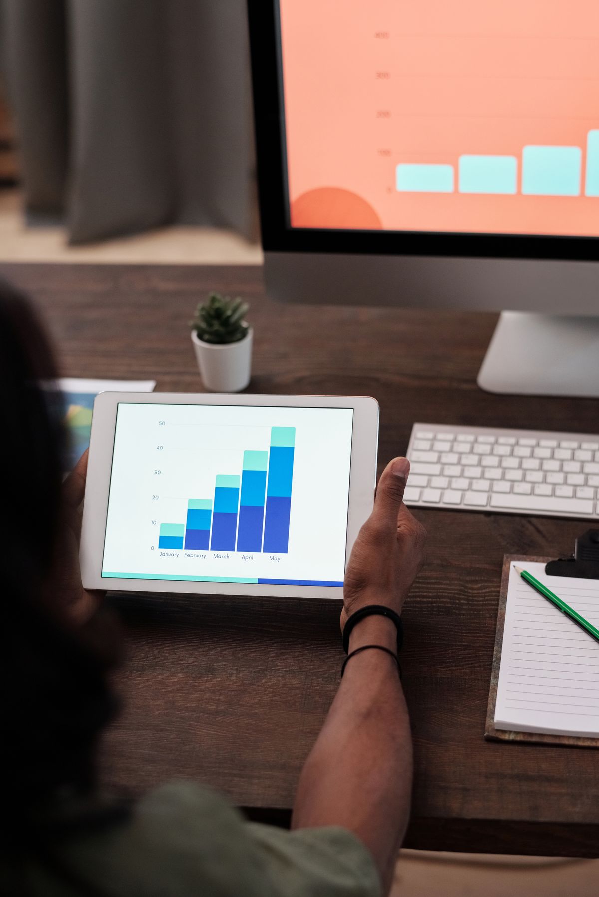 A tablet showing a rising bar chart next to a desktop monitor